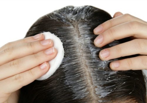 Young woman applying coconut oil onto hair, closeup